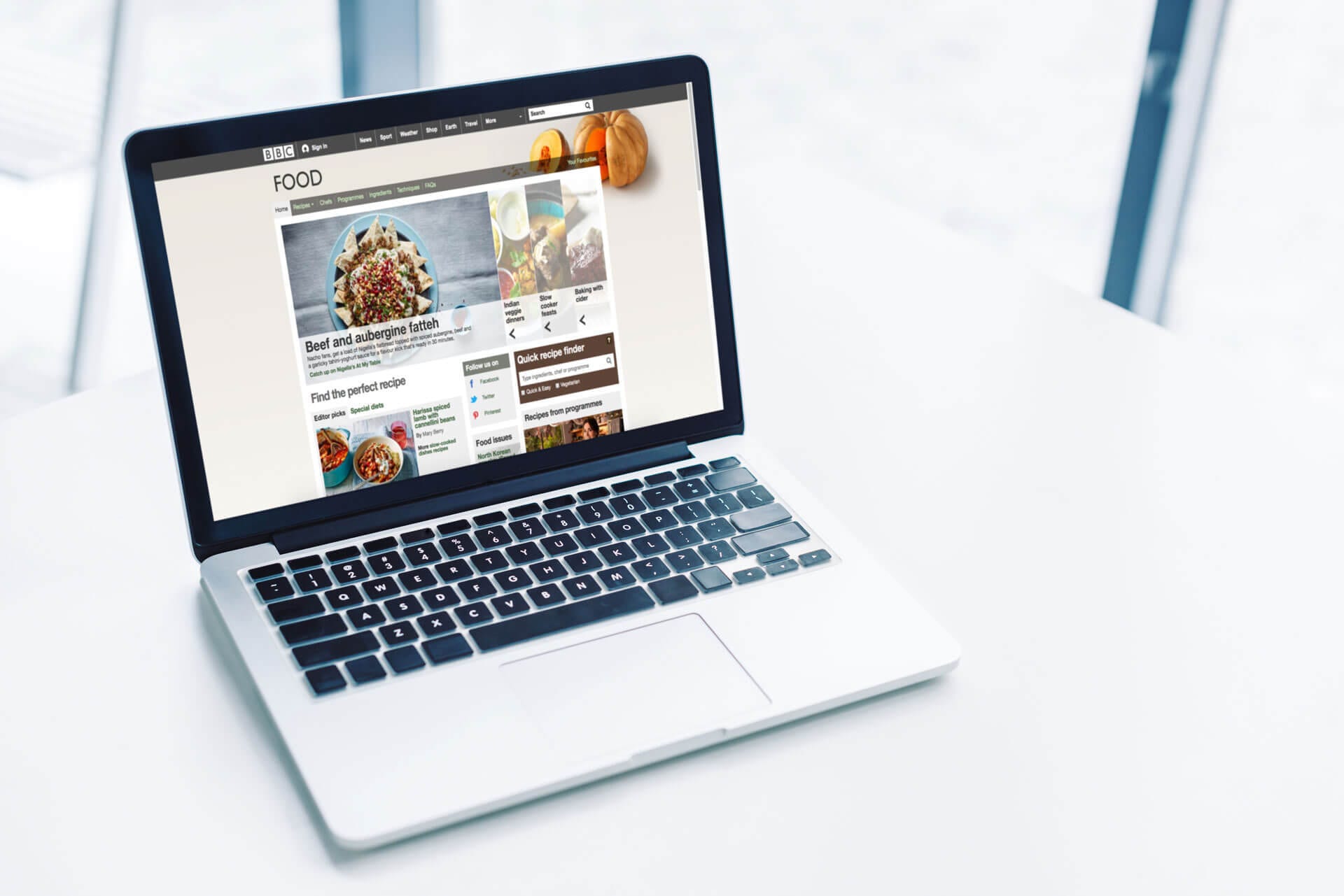 An open laptop placed on a white table, displaying a food website on the screen with various food items and information visible