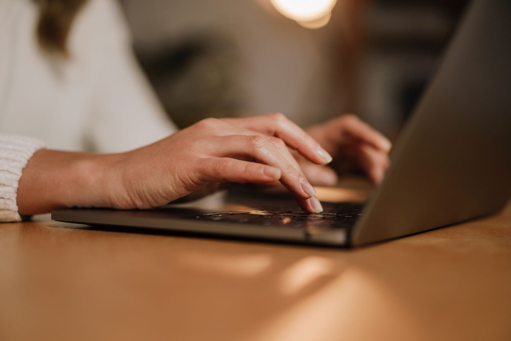 A close-up of the person's hands typing on a laptop keyboard, with only a tiny portion of the person's wrist visible in the frame