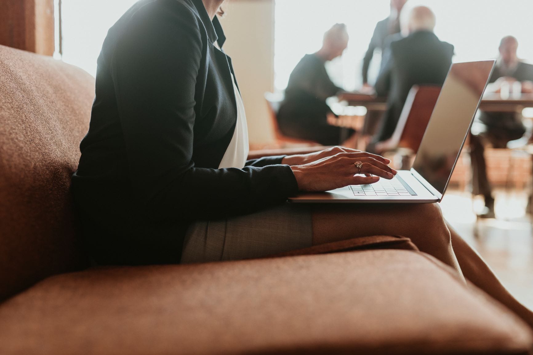 A businesswoman sits with her laptop on her lap, typing on its keyboard in the office with men