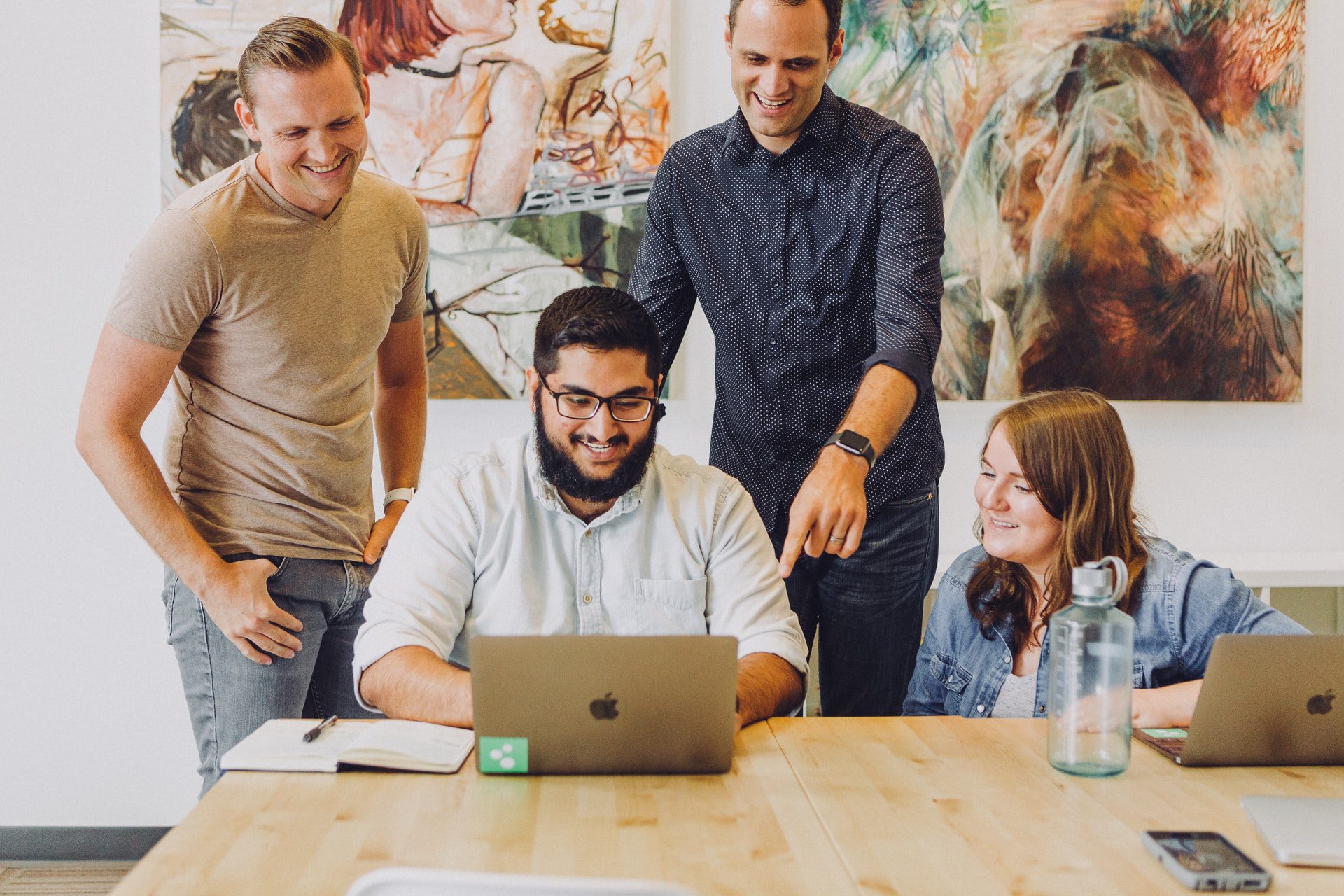 A group of people engaged in a discussion in front of a laptop, with one person pointing at the screen